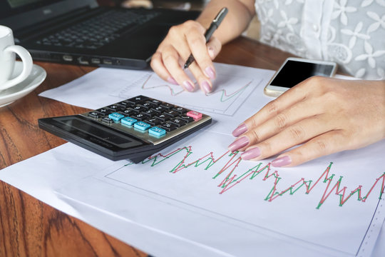 businesswoman hand analyzing stock,financial graph report with calculator,smart phone and notebook on wooden office desk 