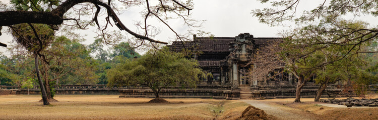 Ancient ruins of temple complex Angkor Wat surrounded by old tropical trees, Siem Reap, Cambodia. Road to the temple in the foreground