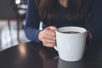 Closeup image of a woman holding and drinking hot coffee in vintage cafe
