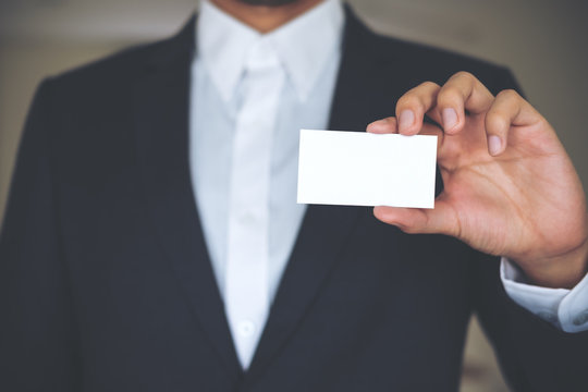 A business man in white shirt and gray suit holding and showing empty business card