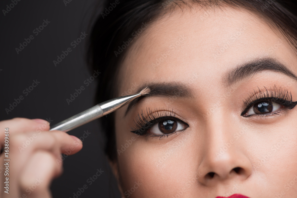 Wall mural close up of beautiful face of young asian woman getting make-up. the artist is applying eyeshadow on