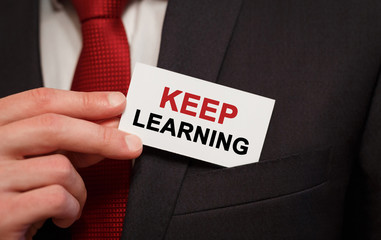 Businessman putting a card with text Keep Learning in the pocket