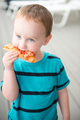 Young toddler boy on patio deck outside at sunset down at shore eating pizza