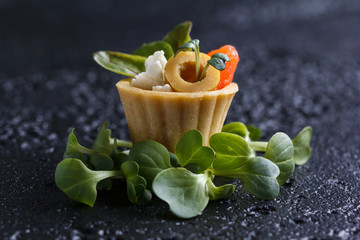 Tartlet with salmon and curd cheese with micro-green on a dark background.