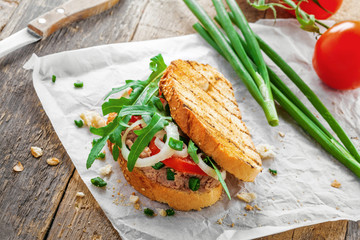 Sandwich made of grilled toasts, tuna salad, tomato, onion and arugula on a table. Delicious healthy meal for lunch.