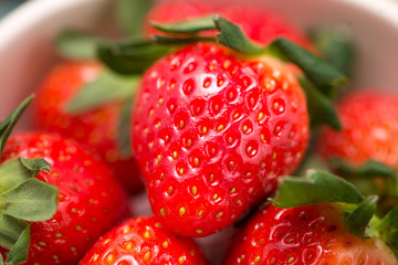 Bowl with fresh strawberry on blue wooden table.