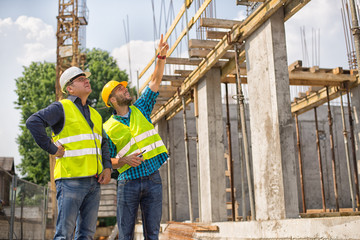 Men in hardhat and green jacket posing on building site