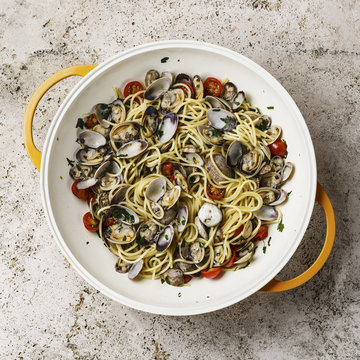 Vongole Shells Clams with tomato and parsley in cooking pan on travertine stone background