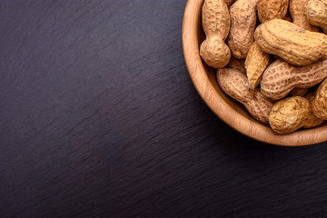 Peanuts lie in a wooden cup on a black stone board in the form of a frame, space for text