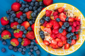 Oatmeal porridge with blueberries, strawberries and muesli on wooden background. Top view. Diet breakfast.