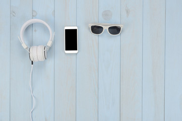 Artículos de ocio sobre fondo de madera azul: auriculares, smart phone y gafas de sol de color blanco