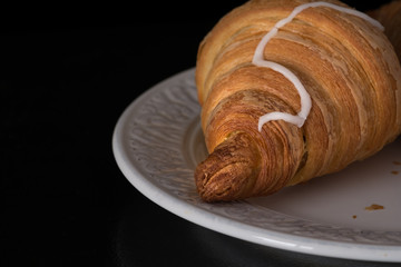 Cinnamon crescent croissant close up view on white plate on black background