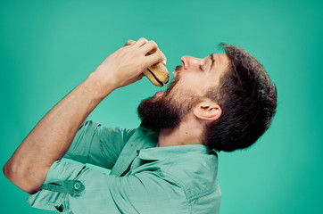 Young guy with a beard on a green background holds a hamburger