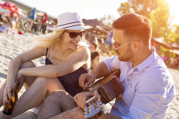 Beautiful loving couple playing guitar on the beach