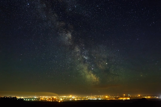 Starry night sky with the Milky Way over the city with lighting.