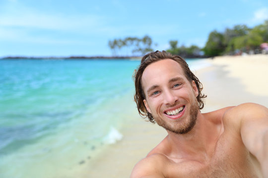 Beach selfie man on summer travel Hawaii vacation vlogging taking self-portrait video or picture as social media vlogger online.