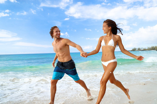 Happy beach vacation couple having fun running splashing water at tropical travel vacations.