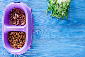 Animal feed in bowl and grass on blue table background top view copyspace