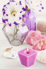 Purple eustoma flowers and lit candle on white table