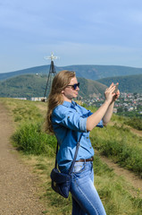 A young girl in blue clothes, wearing sunglasses, takes pictures in the summer on the street