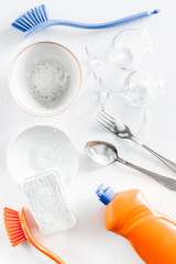 Dishwashing liquid, sponge, brush and tableware on white background top view