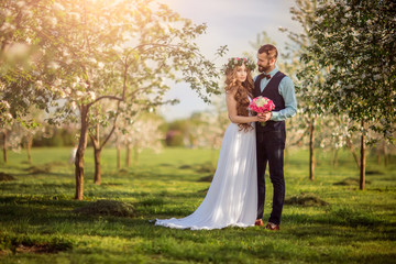 Beautiful bride and a bearded hipster groom embrace in flowered garden. Newlyweds.