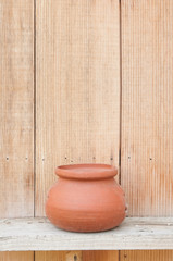 Small clay plant pot on wooden shelf with wood background.