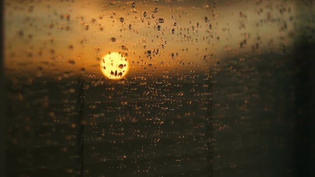 Water drops on a window glass after the rain. The sky with clouds and sun on background.