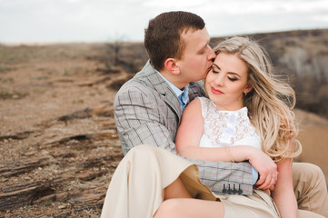 Love, romance and people concept - happy young couple hugging sitting on the edge of a cliff outdoors