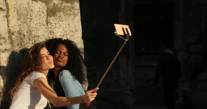 Gorgeous multiethnic girlfriends are sending kisses while taking photos using the selfie stick.