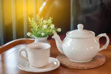 White tea pot and cup with Tea strainer on wooden table, relaxing with hot tea during tea break.
