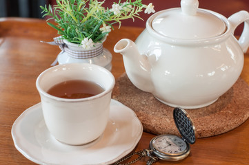 White tea pot and cup with Tea strainer on wooden table, relaxing with hot tea during tea break.