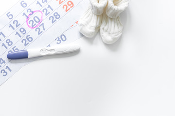 Pregnancy planning. Pregnancy test, calendar and booties on white background top view copyspace