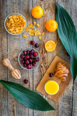 Preparing healthy summer breakfast. Muesli, oranges, cherry, juice on wooden table background top view
