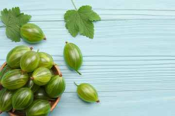 Gooseberry in wooden bowl on blue wooden background. Top view with copy space.