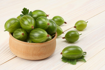 Gooseberry in wooden bowl on white wooden background. 