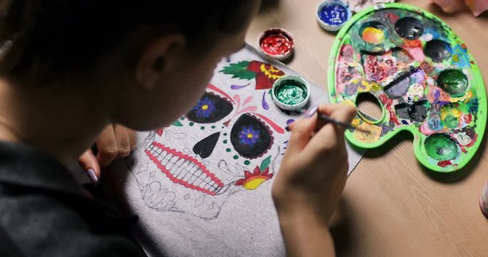 Close-up drawing on clothes. Girl draws on material colorful amazing mexican mask. White T-shirt with a pattern. mexican mask. colorful pattern in process. Creative time in the art studio