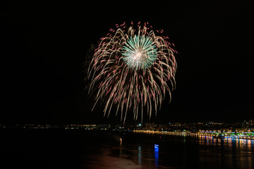 Red, yellow, green fireworks in black night sky over the river