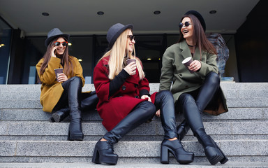 Stylish girls with unusual makeup in trendy coats, scarves, hats and leather shoes on the stairs to...