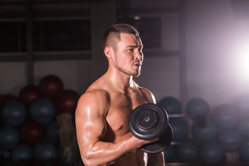 Fototapeta na wymiar Handsome power athletic guy bodybuilder doing exercises with dumbbell. Fitness muscular body on dark background