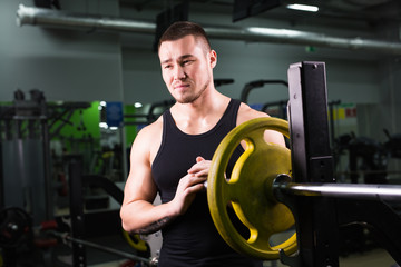 Plakat Young healthy man with big muscles holding disk weights in gym. Fitness, sport, training, motivation and lifestyle concept