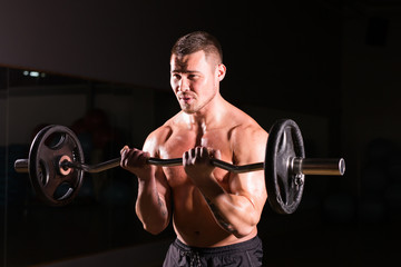 Fototapeta na wymiar Muscular man working out in gym doing exercises with barbell at biceps, strong male naked torso abs