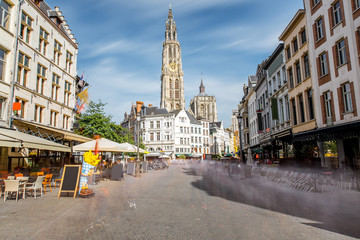 Street view with Our Lady church tower in the center of Antwerpen city, Belgium. Long exposure image technic with motion blurred people and clouds