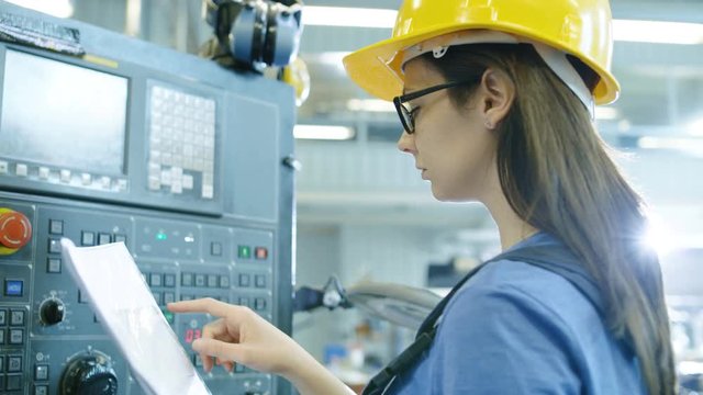 Professional Female Operator in Hard Hat Setting up/ Programming CNC Machine with Control Panel in a Big Industrial Factory. Shot on RED EPIC-W 8K Helium Cinema Camera.