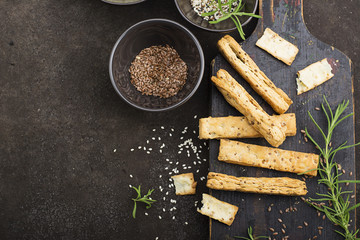 Bread sticks from puff pastry with flax seeds, sesame seeds, sea salt and rosemary on a dark background. Top View.