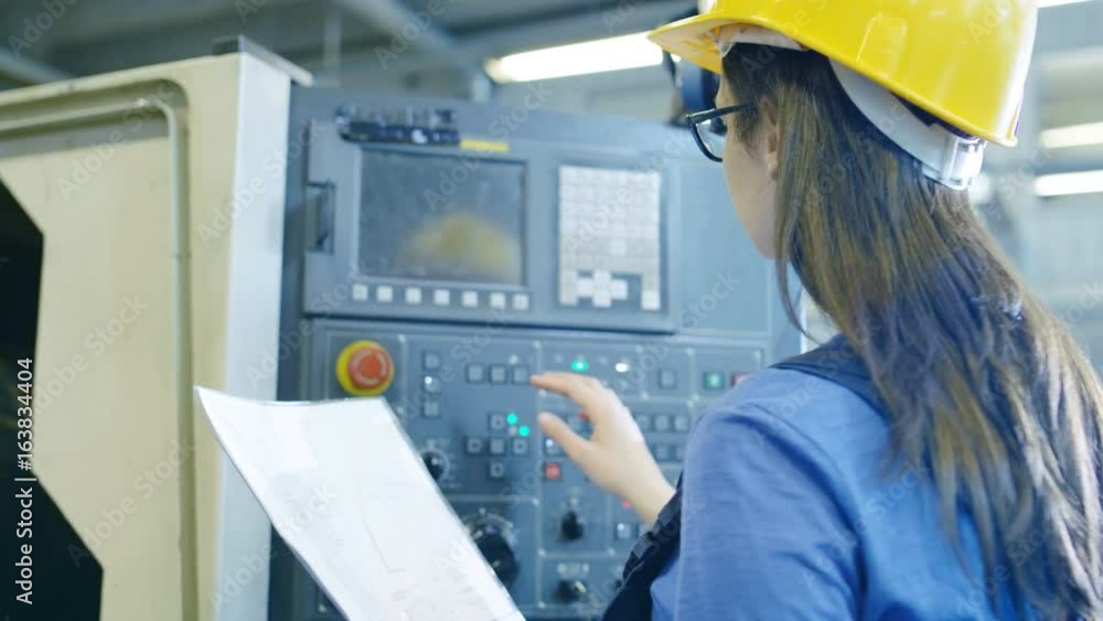 Poster professional female operator in hard hat setting up/ programming cnc machine with help of control pa