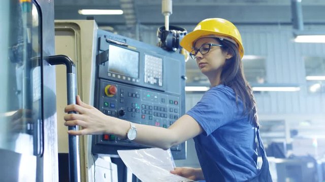Professional Female Operator in Hard Hat Setting up/ Programming CNC Machine with Help of Control Panel. Big Industrial Factory is Visible. Shot on RED EPIC-W 8K Helium Cinema Camera.