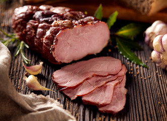 Smoked ham sliced on a wooden rustic table with addition of fresh aromatic herbs.  Natural product...