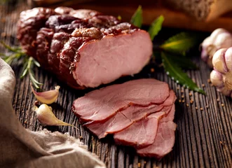 Photo sur Plexiglas Viande Smoked ham sliced on a wooden rustic table with addition of fresh aromatic herbs.  Natural product from organic farm, produced by traditional methods