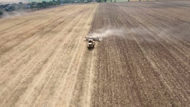 Impressive aerial shot of a big tractor drawing a spike and a disc harrows to remove wheat straw and to do a  tillage in Eastern Europe in a sunny day. The drone is flying in front of a tractor